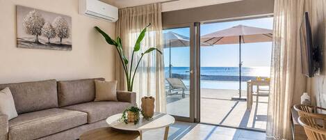 A modern living room with a sofa, a small round table, and a large window with a view of the beach.