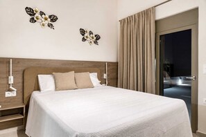 A hotel room with a large bed, two wall-mounted lamps, a wooden headboard, and a view of the street through a glass door. - Azzurro Luxury Villa 1 (Rhodes)