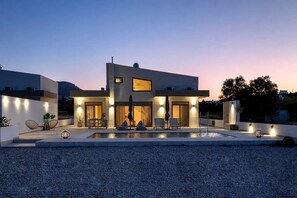 A modern two-story house with a swimming pool, outdoor seating, and a well-lit entrance. - Azzurro Luxury Villa 1 (Rhodes)