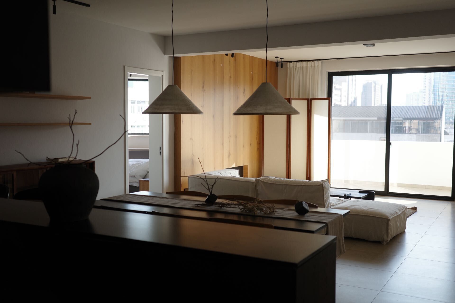 A modern living room with a large window, a sofa, a coffee table, and a dining area.
