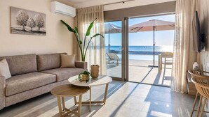 A modern living room with a sofa, a small round table, a large potted plant, and a view of the beach through a glass door. - Azzurro Luxury Villa 2 (Rhodes)