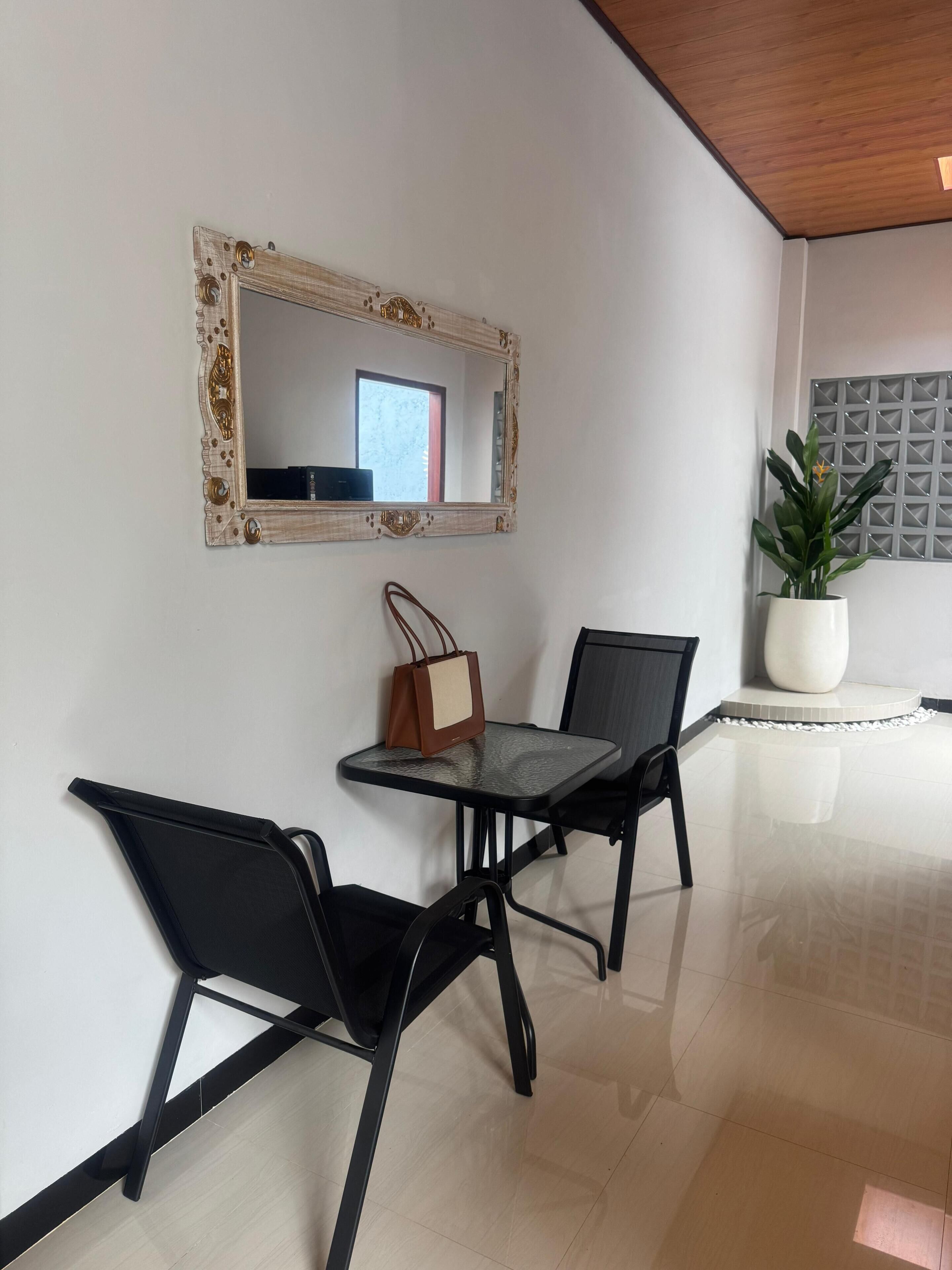 Een kamer met een spiegelwand, een tafel met stoelen, een potplant en een handtas op tafel.