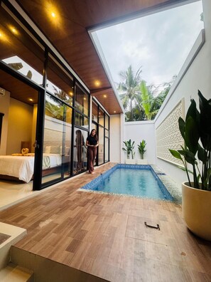 A modern hotel room with a glass wall, a small pool, and a wooden floor.