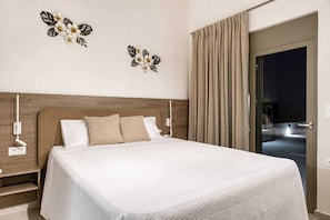 A hotel room with a large bed, two wall-mounted lamps, a wooden headboard, and a view of the street through a glass door. - Azzurro Luxury Villa 4 (Rhodes)