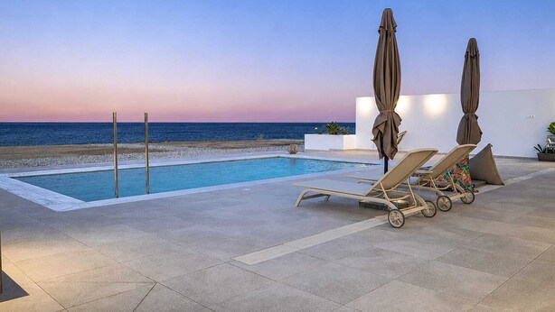 A poolside area with lounge chairs and umbrellas, overlooking a beach and ocean. - Azzurro Luxury Villa 4 (Rhodes)