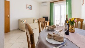 Un coin repas avec une table dressée pour deux personnes, un canapé et un téléviseur en arrière-plan.