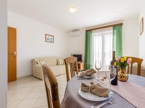 A dining area with a table set for two, a sofa, and a television in the background. - Apartments Anamarija - One Bedroom Apartment With Balcony - 4 (Privlaka)