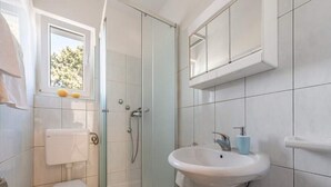 Une salle de bain comprenant des toilettes, une douche fermée par des parois de verre et un lavabo.