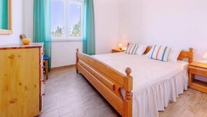 Une chambre à coucher avec un lit en bois, une table de chevet, une commode et une fenêtre avec des rideaux.