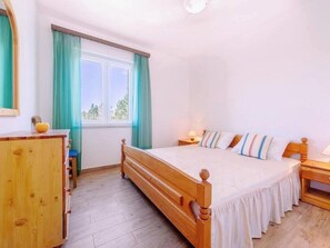 A bedroom with a wooden bed, a nightstand, a dresser, and a window with curtains. - Apartments Anamarija - One Bedroom Apartment With Balcony - 4 (Privlaka)