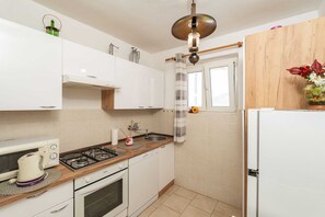 Eine kleine Küche mit weißen Schränken, einem Gasherd, einem Backofen, einer Spüle und einem Kühlschrank.
