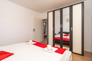 A hotel room with a bed, a red bedspread, a white towel, and a wardrobe with a mirror.