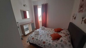 Une chambre à coucher avec un lit, une commode, un miroir et une fenêtre avec des rideaux.
