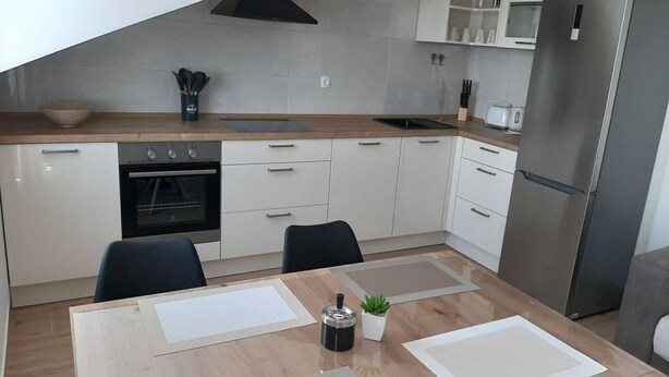 Une cuisine moderne avec des meubles blancs, un réfrigérateur en acier inoxydable et une table à manger agrémentée de sets de table.