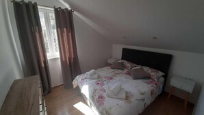 Une chambre à coucher avec un lit, des rideaux, une table de chevet et une commode en bois.