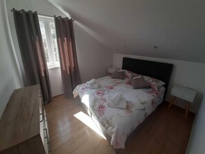 Ein Schlafzimmer mit einem Bett, Vorhängen, einem Nachttisch und einer Holzkommode.