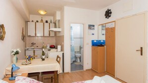 A compact room with a bed, a small table with a bottle and glasses, a kitchenette with cabinets, a bathroom with a toilet, and a wardrobe. - Apartment Stella Polaris - Studio Apartment A2 (Dubrovnik)