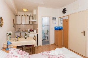 A compact room with a bed, a small table with a bottle and glasses, a kitchenette with cabinets, a bathroom with a toilet, and a wardrobe. - Apartment Stella Polaris - Studio Apartment A2 (Dubrovnik)