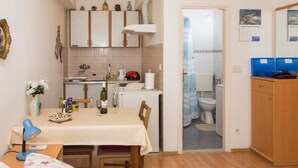 A compact kitchen with a dining area, a small table with a lamp, and a view into the adjacent bathroom. - Apartment Stella Polaris - Studio Apartment A2 (Dubrovnik)