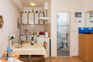 A compact kitchen with a dining area, a small table with a lamp, and a view into the adjacent bathroom. - Apartment Stella Polaris - Studio Apartment A2 (Dubrovnik)