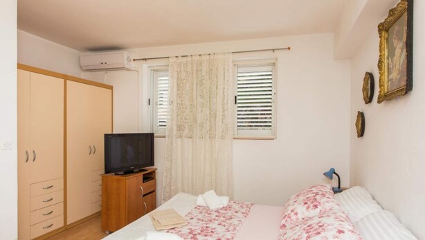 A bedroom with a bed, a TV, a wardrobe, and a window with curtains. - Apartment Stella Polaris - Studio Apartment A2 (Dubrovnik)