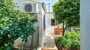 A narrow courtyard with a tiled floor, a wooden table and chairs, and a tree. - Apartment Vulicevic A2 (Dubrovnik)
