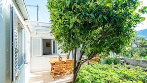 A patio with a table and chairs, a tree, and a garden with plants. - Apartment Vulicevic A2 (Dubrovnik)