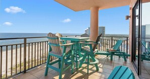 A balcony with a view of the beach and ocean, featuring outdoor furniture and a glass door.