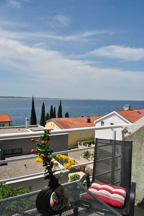 A balcony with a view of the sea, a chair with a red and white cushion, and a vase with yellow flowers. - Apartments Smokvica - Superior One Bed /apt (Starigrad)