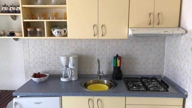 A kitchen with a gas stove, sink, and a coffee maker. There are cabinets with handles and a shelf above the sink. - Apartments Paloc - One-bedroom Apartment With Balcony (Bol)