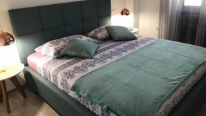 A neatly made bed with a patterned bedspread, a green headboard, and two bedside lamps. - Apartments Paloc - One-bedroom Apartment With Balcony (Bol)