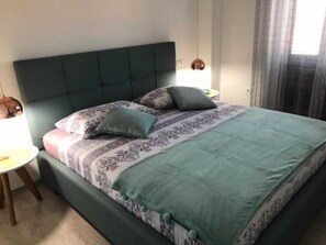 A neatly made bed with a patterned bedspread, a green headboard, and two bedside lamps. - Apartments Paloc - One-bedroom Apartment With Balcony (Bol)