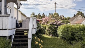 Una casa de madera con un porche, una escalera que lleva a la entrada, y un jardín con diversas plantas y flores.
