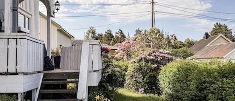 A wooden house with a porch, a staircase leading to the entrance, and a garden with various plants and flowers.