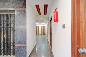 A corridor with a fire extinguisher mounted on the wall, a metal gate on the left, and wooden doors at the end. - Super Collection O Gachibowli Phase 2 (Hyderabad)