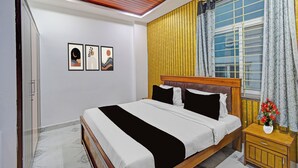 Un dormitorio con cama, mesita de noche, ventana con cortinas y dos obras de arte en la pared.