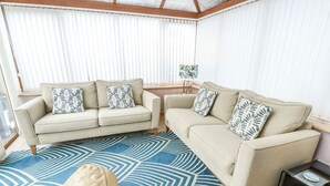 A living room with two beige sofas, patterned throw pillows, a blue geometric rug, and a small side table with a lamp. - 1 The Old Smithy (Cemaes Bay)