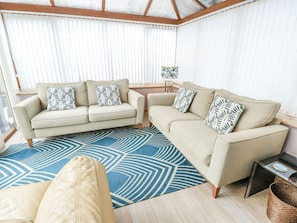 A living room with two beige sofas, patterned throw pillows, a blue geometric rug, and a small side table with a lamp. - 1 The Old Smithy (Cemaes Bay)