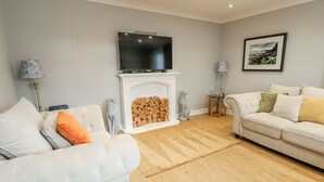 A living room with a fireplace, a television mounted above it, and two sofas with cushions. - 1 The Old Smithy (Cemaes Bay)