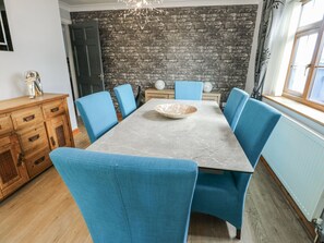 A dining area with a marble table, blue upholstered chairs, a stone wall, and a wooden cabinet. - 1 The Old Smithy (Cemaes Bay)