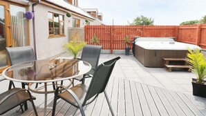 A patio with a round table and chairs, a hot tub, and a wooden deck. - 1 The Old Smithy (Cemaes Bay)