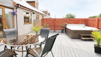 A patio with a round table and chairs, a hot tub, and a wooden deck.