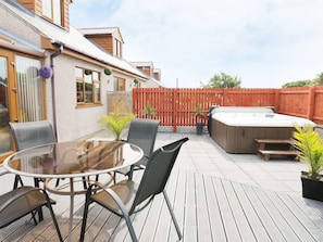 A patio with a round table and chairs, a hot tub, and a wooden deck. - 1 The Old Smithy (Cemaes Bay)