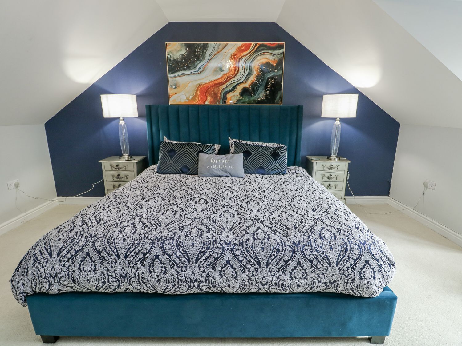 Un dormitorio con cama, dos mesitas de noche, un cuadro colgado en la pared y un techo con diseño triangular.