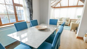 A dining area with a table and chairs, a large window, and a view of a living room. - 1 The Old Smithy (Cemaes Bay)