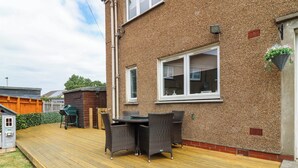 A wooden deck with outdoor furniture, a brick house, and a small shed. - 6 Niddrie Marischal Road (Edinburgh)
