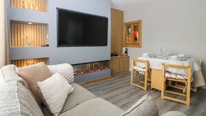 A modern living room with a large flat-screen TV, a fireplace, a dining area with a wooden table and chairs, and a sofa with patterned cushions. - 6 Niddrie Marischal Road (Edinburgh)
