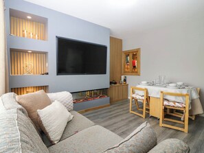 A modern living room with a large flat-screen TV, a fireplace, a dining area with a wooden table and chairs, and a sofa with patterned cushions. - 6 Niddrie Marischal Road (Edinburgh)