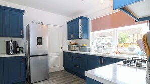 A modern kitchen with blue cabinets, a stainless steel refrigerator, and a window with a view of the outside. - 6 Niddrie Marischal Road (Edinburgh)