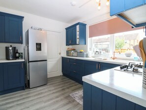 A modern kitchen with blue cabinets, a stainless steel refrigerator, and a window with a view of the outside. - 6 Niddrie Marischal Road (Edinburgh)